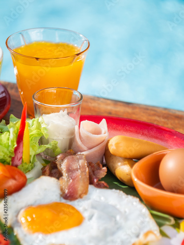 Breakfast set on wooden table with blue background of water in pool.