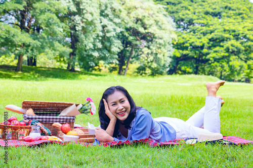 Young Asian woman relax time in park.In the morning she is sipping tea , smile and  laugh .She is  lying on the grass beside picnic basket. © Teerayut