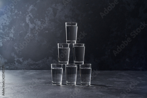Pyramid of glasses of vodka on a black background, selective focus