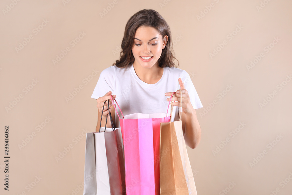 Cheerful young girl in basic clothes while holding shopping bags isolated over beige background.