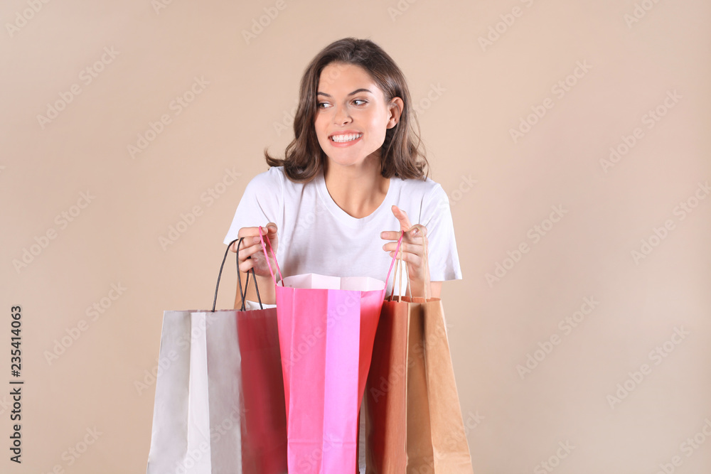 Cheerful young girl in basic clothes while holding shopping bags isolated over beige background.