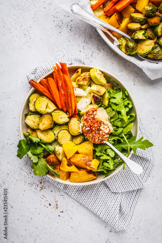 Baked brussels sprouts, zucchini, pumpkin, carrots and hummus salad in a white dish.