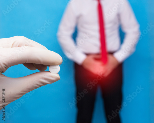 doctor with a pill in his hand from sexually transmitted diseases, in the background a man clings to the lower abdomen he has genital infection and prostate cancer