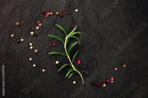 A photo of an elegant rosemary branch with peppercorns, shot from the top on a black background with a place for text