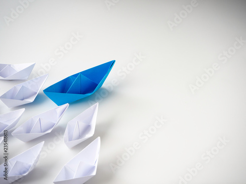 Blue paper boat leading among white ships