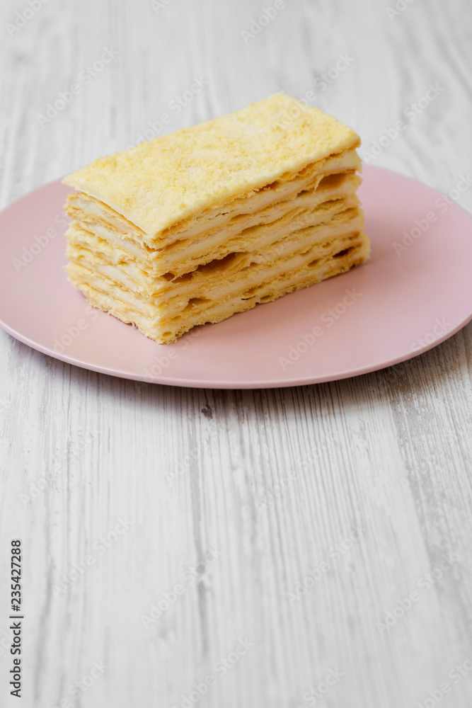 Piece of Napoleon Cake on pink plate over white wooden background, close-up. Piece of Napoleon Cake on pink plate over white wooden background, close-up.