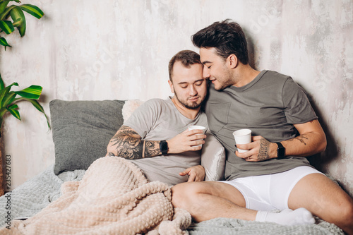 European happy gay couple drinking tea while having fun in bed , caressing and watching movies. Homosexual relationships and alternative love lifestyle concept photo