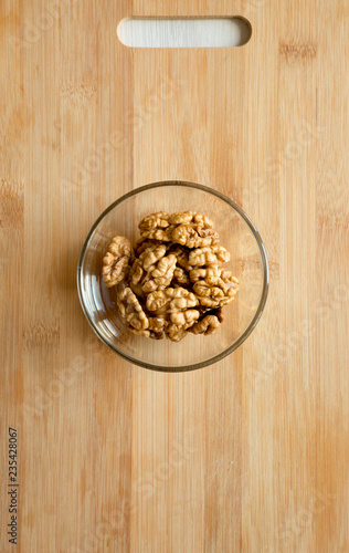Walnuts in glass bowl on bamboo board, top view. Flat lay, overhead, from above.