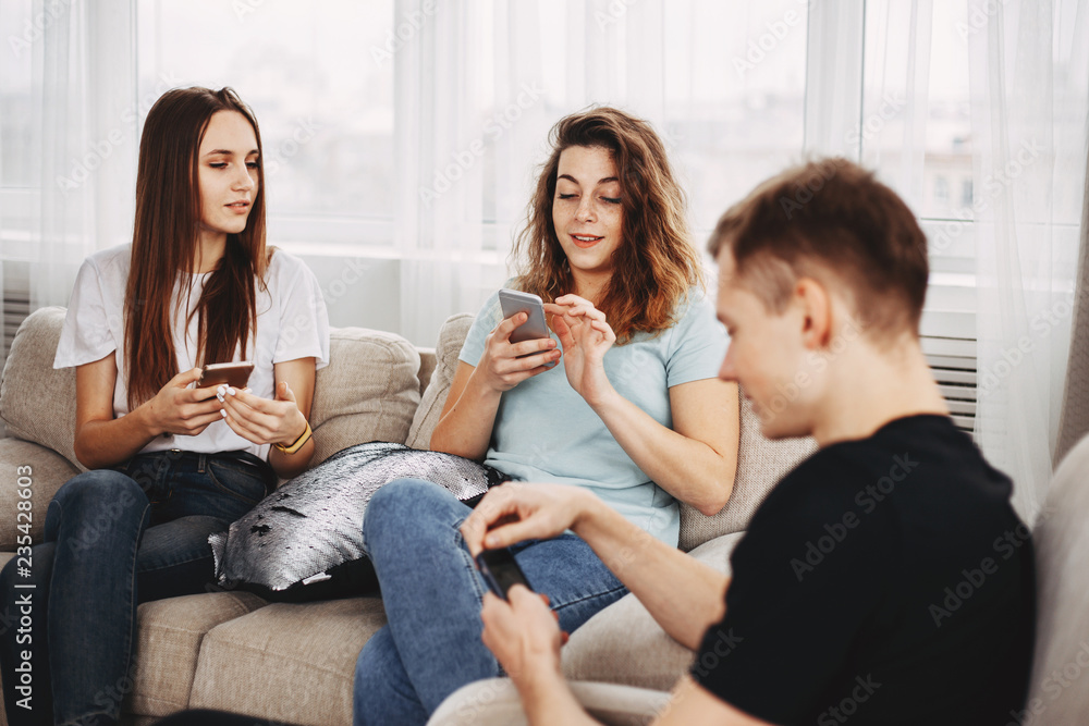 company of young friends talking and using smartphones apps on wifi in living room, happy millennial people having fun with phones company of young friends talking and using smartphones apps on wifi in living room, happy millennial people having fun with phones