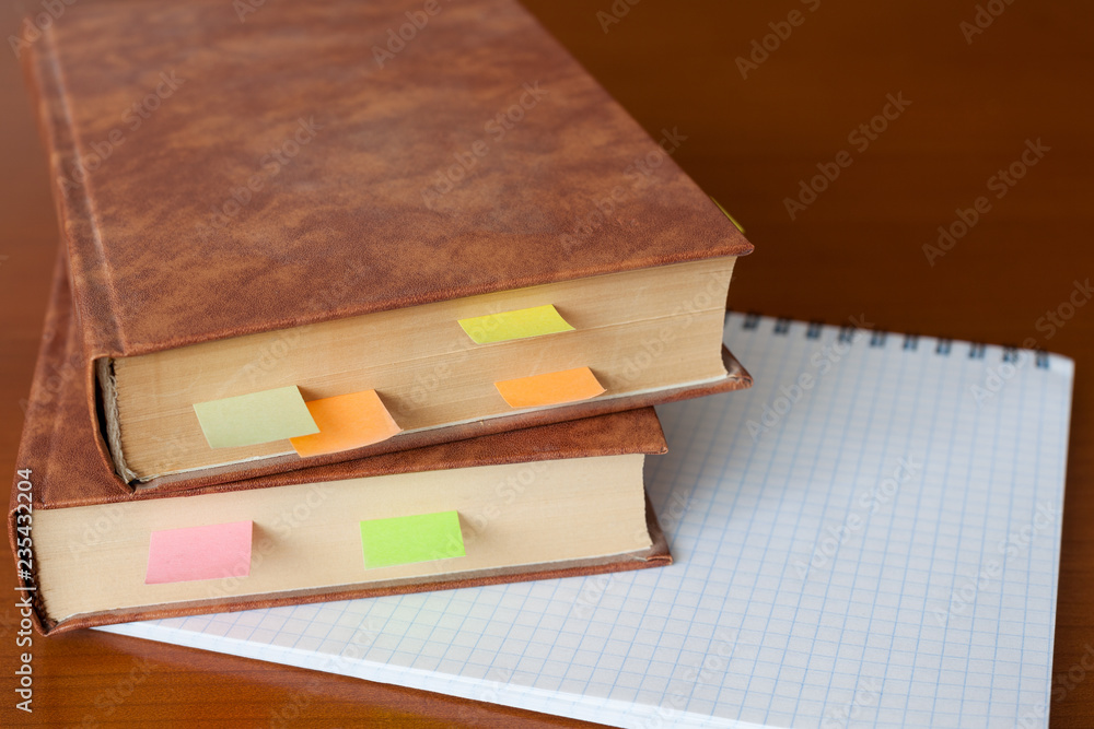 A stack of old books with bookmarks and a squared notebook on a wooden table. Copy space. A stack of old books with bookmarks and a squared notebook on a wooden table. Copy space.