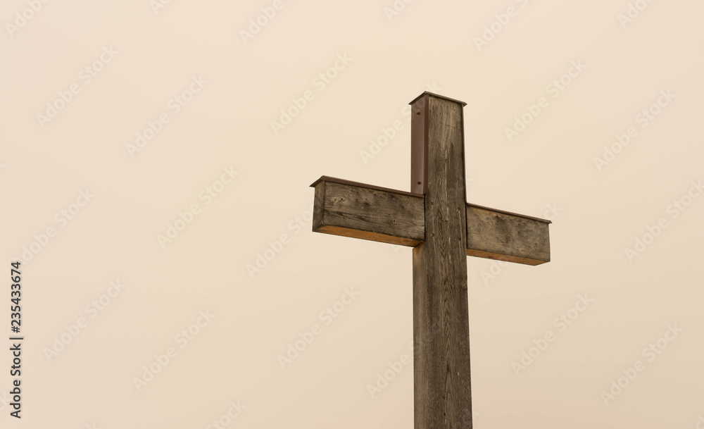 Simple oak wooden cross on natural light, dense fog on the slightly orange background from the sun. Simple oak wooden cross on natural light, dense fog on the slightly orange background from the sun.