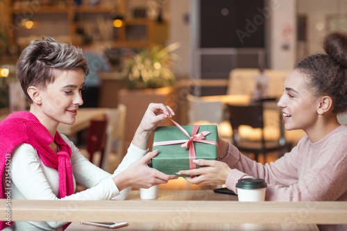 Foto Happy caucasian woman congratulates her female friend with present box while sitting in mall cafe