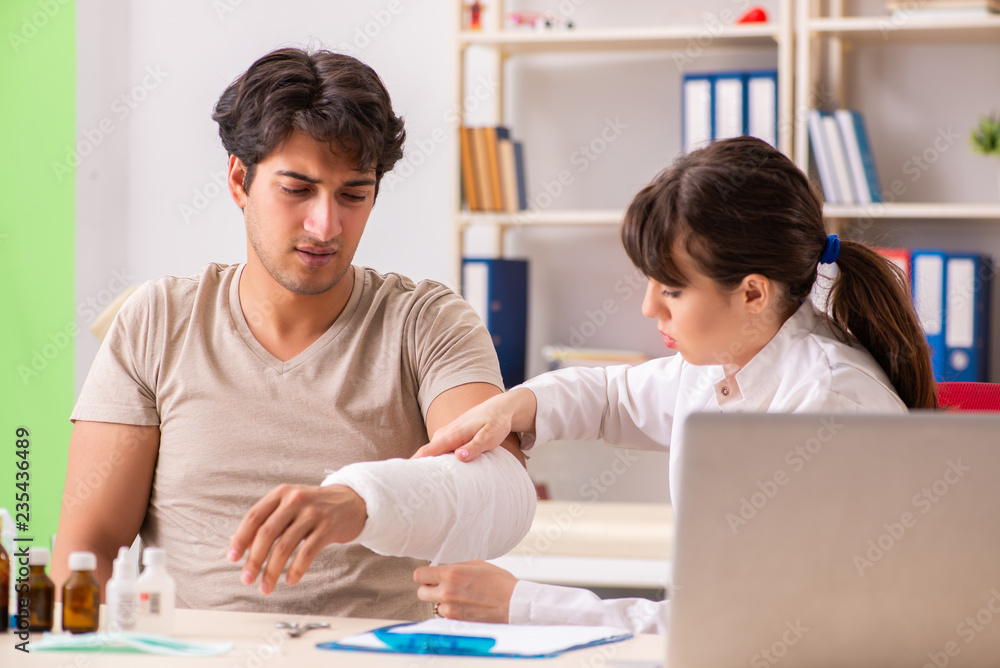 Young man with bandaged arm visiting female doctor traumatologis Young man with bandaged arm visiting female doctor traumatologis