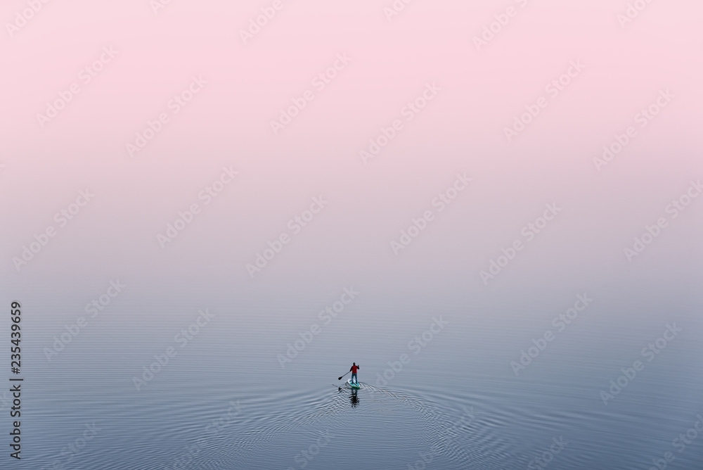 SUP Surfing,View From Above: Lonely Man Is Training On Sup Board On A Large Lake During Pinky Sunset. Surfer.Man In Red Jacket Stand On Sup Paddle Board, Exercising On The Alpine Lake In Mongolia