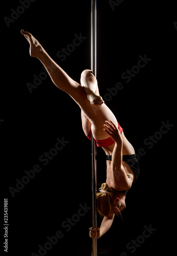 Woman performs pole dance on the stage. Girl whirls around the pole while performing dance or yoga  in the studio. Blonde lady dancing a striptease