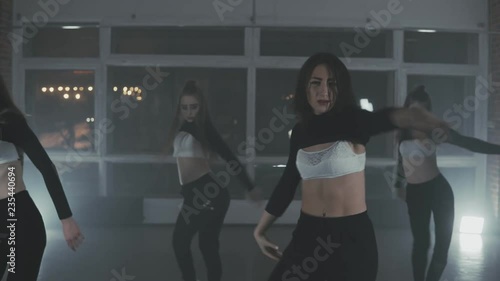 Girls enjoying funky hip hop moves in dark studio with smoke and lighting. Group of young hip-hop dancers performing on the stage. Happy dancing women. Medium shot photo