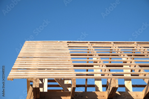 Process of wooden carcass house mounting ubder clear cloudless blue sky side view. Wooden country house construction