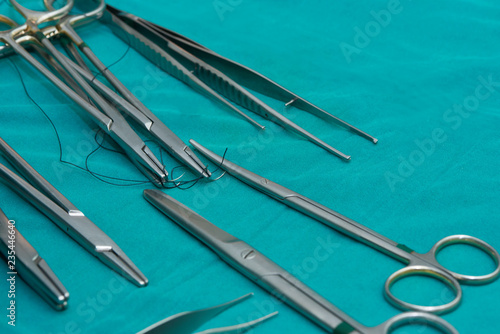 Close-up of needle holders with needles and sutures, surgical forceps and scissors on operating table