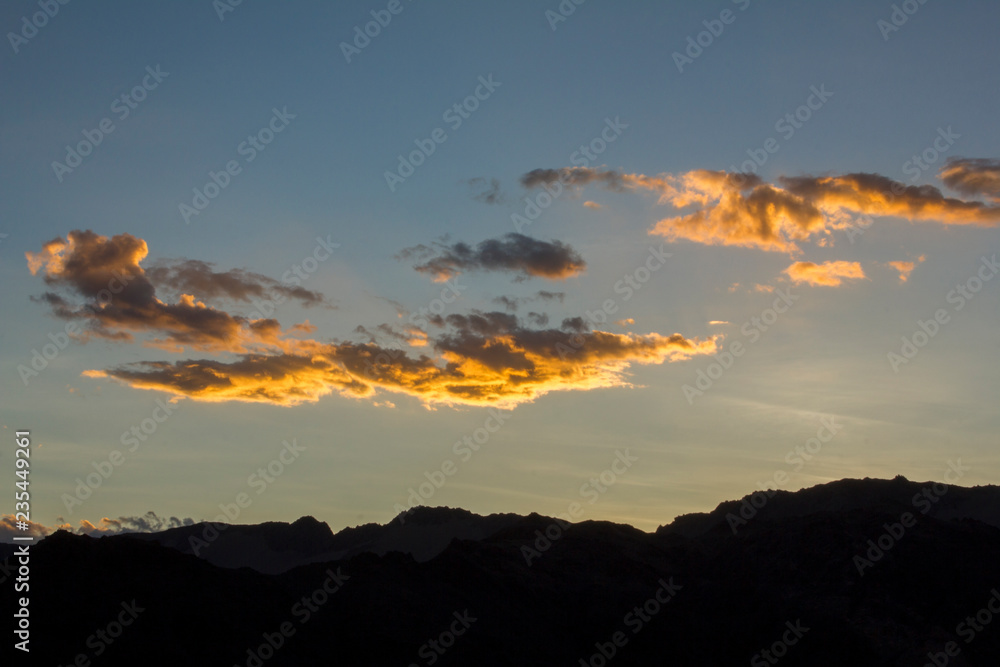 bright white yellow orange clouds in a sunset dark blue sky over the black silhouettes of the mountains