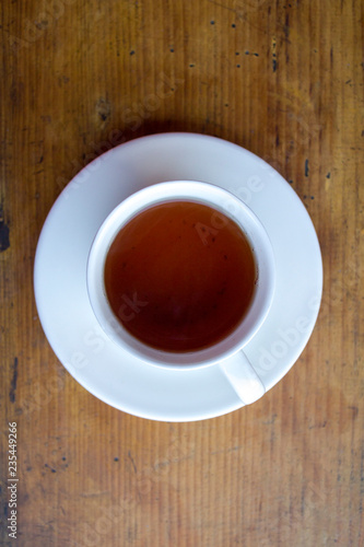 black tea in a white mug on a saucer on the wooden surface of the table top view