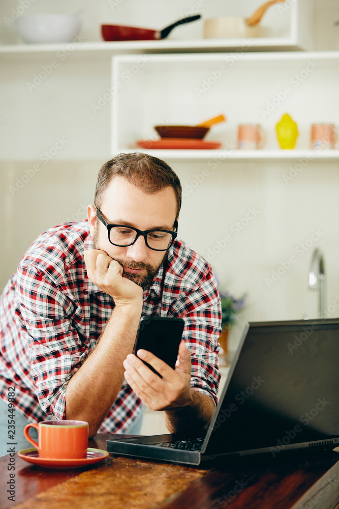Modern bearded man using cellphone and drinking coffee with laptop. Modern bearded man using cellphone and drinking coffee with laptop.