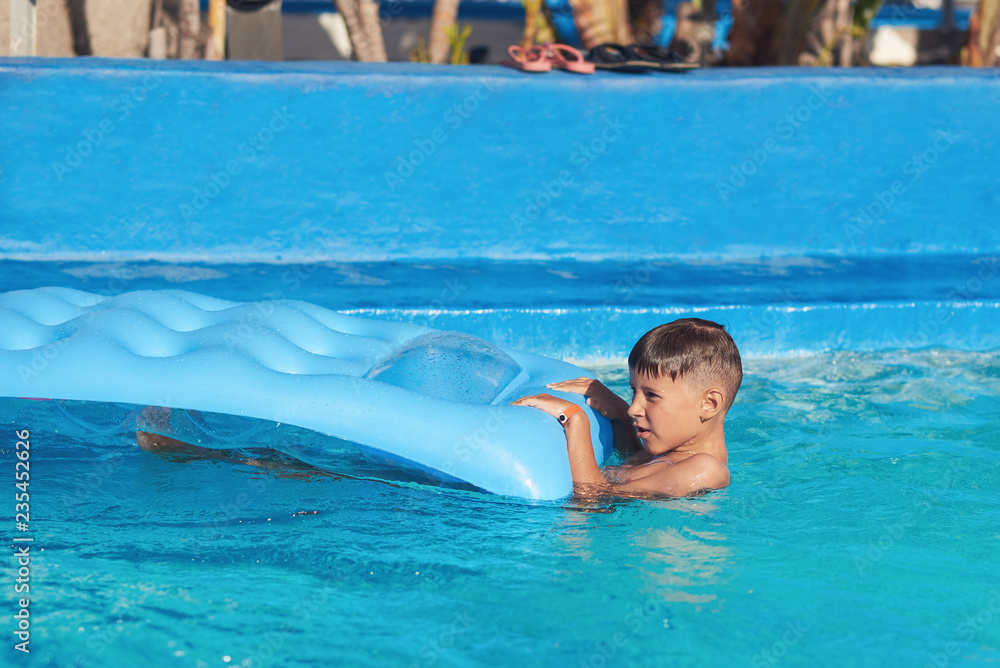 Caucasian boy having fun in swimming pool at resort. He is using inflatable mattress.