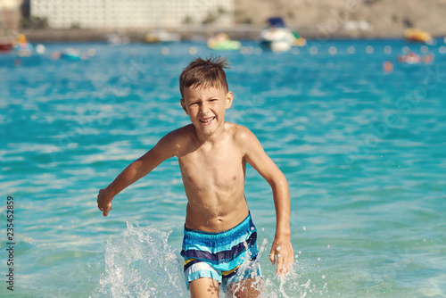 European boy is having fun in the sea cost. He is running from the water and enjoying his summer holidays.