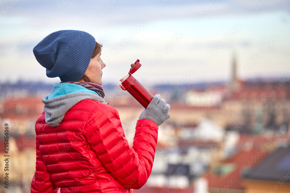 Fototapeta premium Prague. A girl enjoys a bird's-eye view of the old town and drinks a warm drink from a thermos.