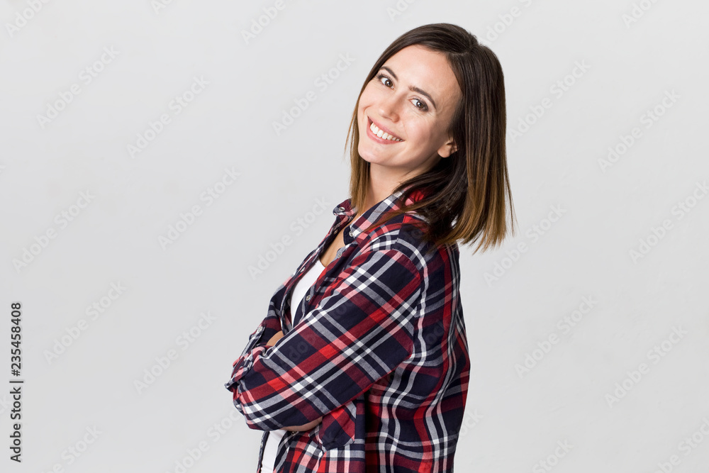 Smiling positive female with attractive look, wearing checkered shirt, posing against white blank wall Smiling positive female with attractive look, wearing checkered shirt, posing against white blank wall