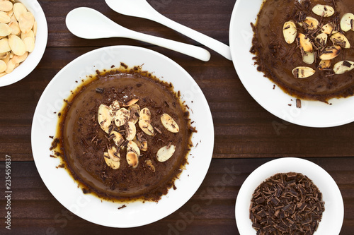 Chocolate pudding or flan dessert with caramel sauce, roasted almond slices and chocolate shavings, photographed overhead with natural light (Selective Focus, Focus on the top of the desserts)