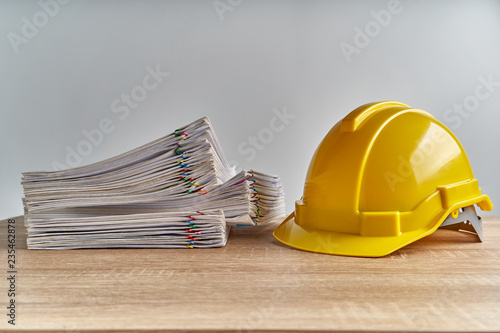 Stack overload document of report with yellow engineer hat