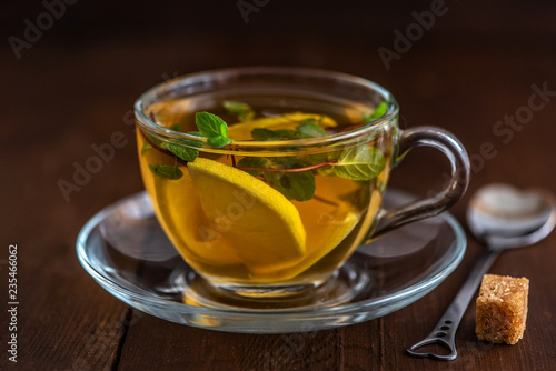 Cup of Lemon tea with lemon slices, cane sugar and mint on dark wooden background