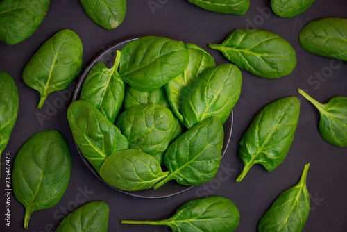 Fresh spinach leaves in bowl on dark background. Top view