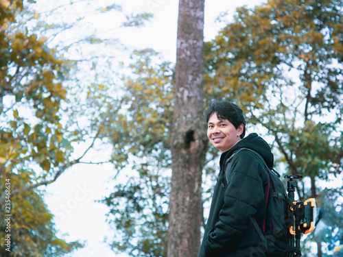 solo backpack and camping concept from backside of black hair man in warm hoodie sweatshirt with his bag solo travel, relax, happy and see to forest and mountain in morning after sunrise