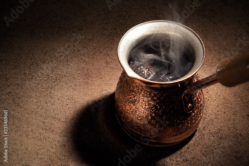Boiling coffee in copper Turkish coffee brewing pot on the sand photo