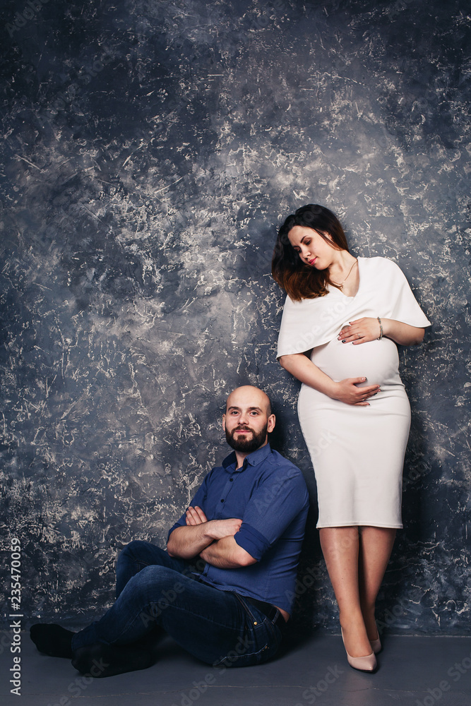 the happy young pregnant couple in the studio on a dark background. family relationship concept. the happy young pregnant couple in the studio on a dark background. family relationship concept.