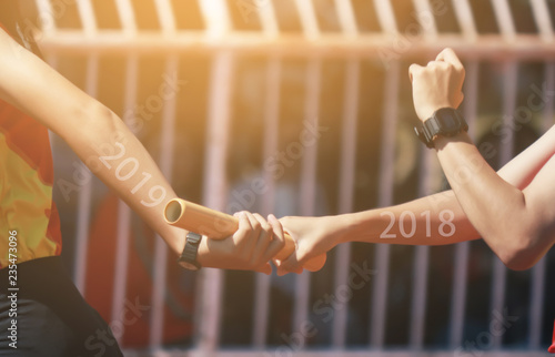 Professional Athlete passing a baton to the partner against race on racetrack.between 2018 and 2019 years.happy new year 2019.
