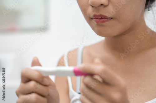 Unhappy young asian woman holding pregnancy test showing a negative result in her bathroom  wellness and healthy concept  infertility problem Selective focus.