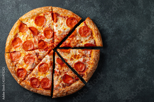 Tasty pepperoni pizza and cooking ingredients tomatoes basil on black concrete background. Top view of hot pepperoni pizza. With copy space for text. Flat lay