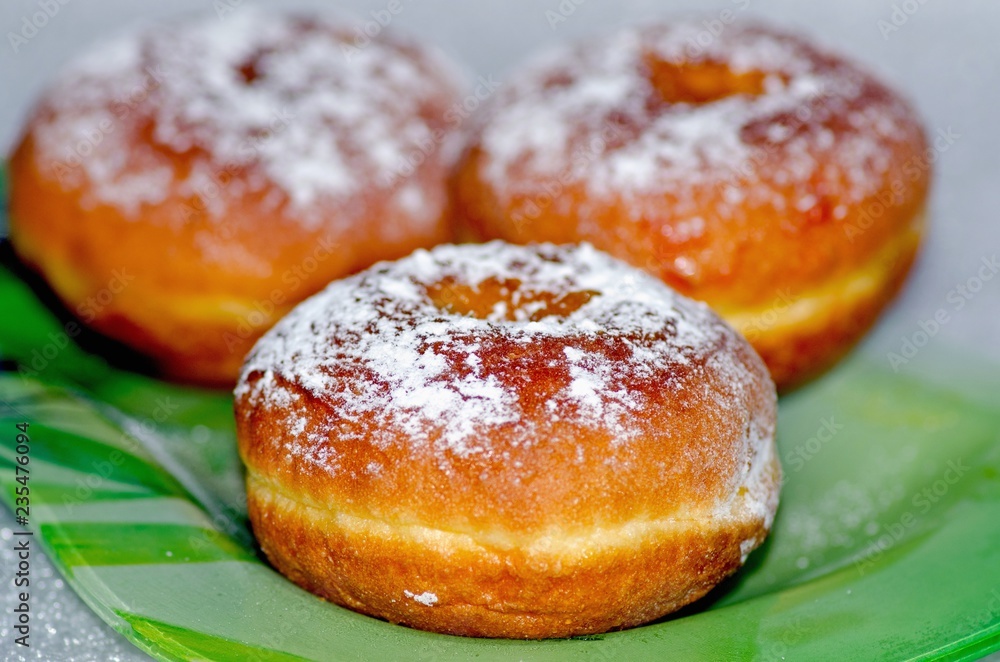 Sweet tasty donuts sprinkled with powdered sugar lie on a green glass plate, the national dish for the holiday of Hanukkah