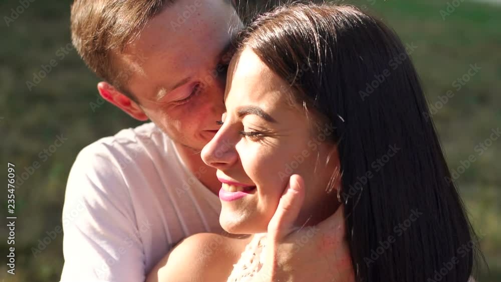 A beautiful young couple sitting on the grass in a park near a tree, they tenderly look at each other laughing and kissing. A beautiful young couple sitting on the grass in a park near a tree, they tenderly look at each other laughing and kissing.