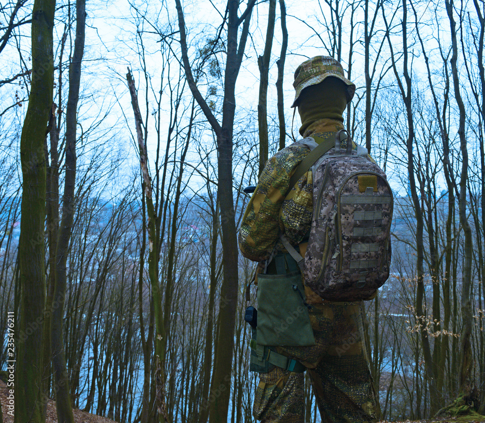 Rear view of military young man with backpack on cold dark forest background.