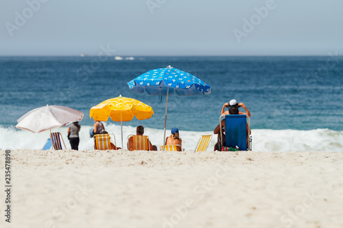 Fototapeta Naklejka Na Ścianę i Meble -  Group of people under their umbrellas facing the sea on a beach seen from behind