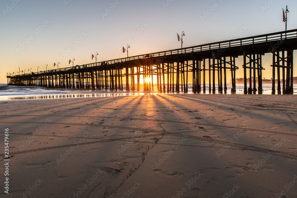 Obraz premium Sunset shining through the pier wooden pilings like spokes of a wagon wheel during this Autum Southern California evening.