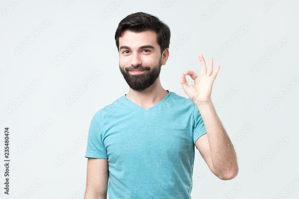 Gesturing OK sign. Cheerful hispanic young man in t-shirt showing approving sign. Good choice concept Gesturing OK sign. Cheerful hispanic young man in t-shirt showing approving sign. Good choice concept