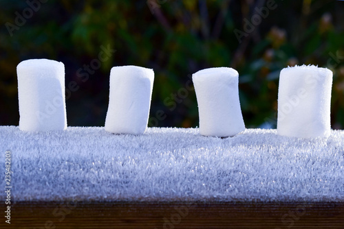 4 pieces of marshmallows stand in the snow in a row. Traditional New Year sweets. photo