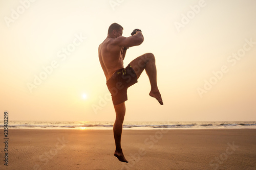 Strong boxer shirtless coach during kickboxing exercise with trainer in boxing gloves at sunset.sports figure, perfect abdominal muscles motivation