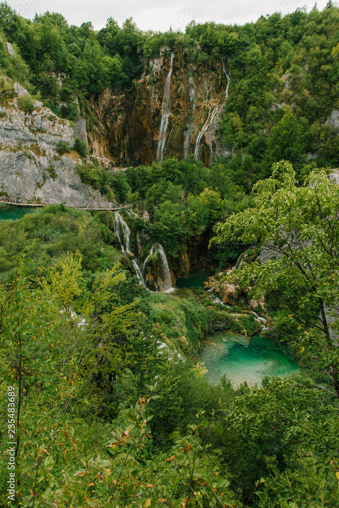 Travel to Croatia. Plitvice Lakes is a popular Croatian national park of incredible beauty. Photo of a favorite point among tourists - a stunning waterfall surrounded by greenery Travel to Croatia. Plitvice Lakes is a popular Croatian national park of incredible beauty. Photo of a favorite point among tourists - a stunning waterfall surrounded by greenery