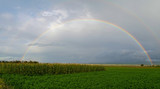 Full rainbow above farm fields with a cloudy sky