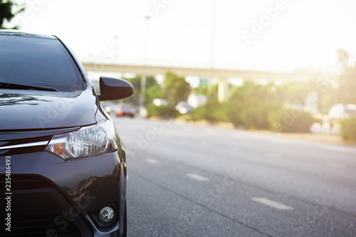 Focusing on the Dark Gray car headlights on a street corner with sunlight flares, In the background, the driver, bike and car. Closeup headlights of car. Copy space for insert text.